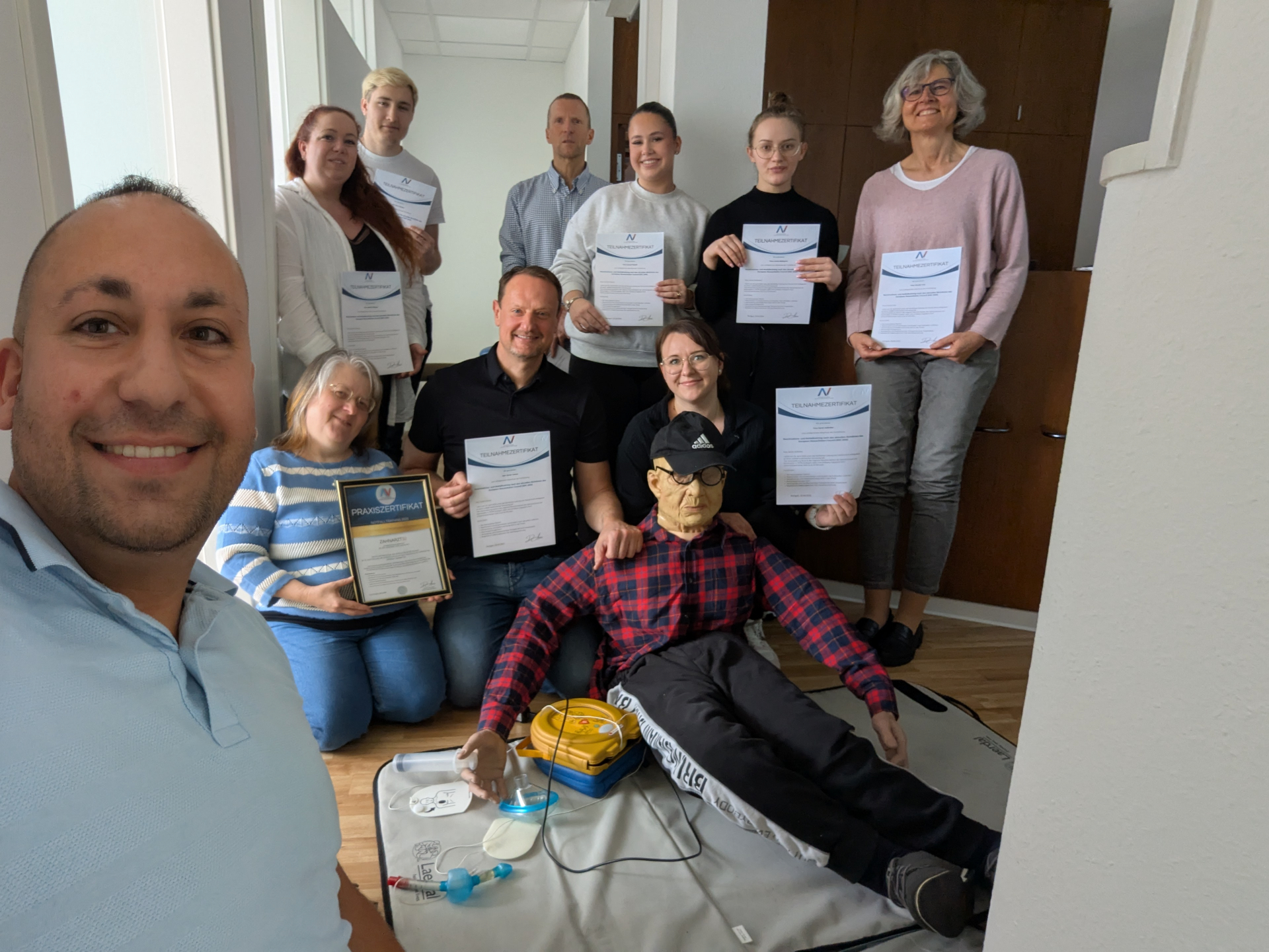 Praxisteam mit Teilnahmezertifikaten nach dem Notfalltraining – mit Reanimationsphantom und AED
