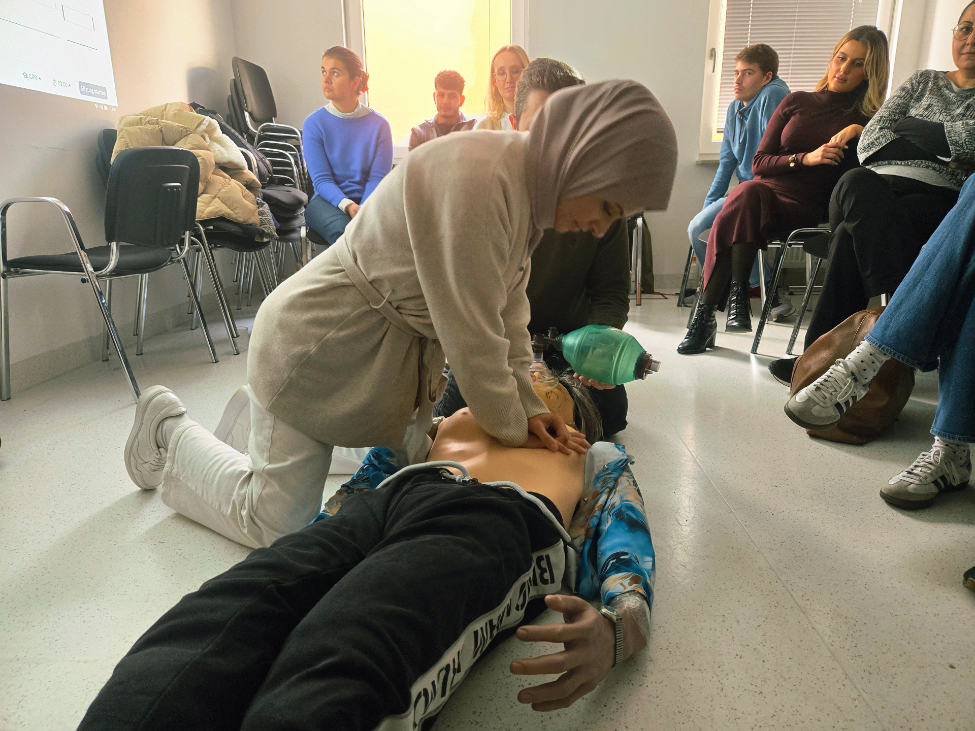 Zwei-Helfer-Reanimation mit Beutel-Masken-Beatmung vor zuschauender Schulungsgruppe