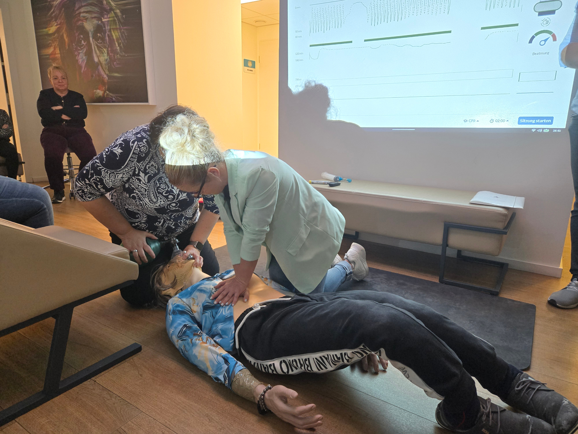 Zwei-Helfer-Reanimation im Praxisraum mit QCPR Live-Feedback an der Wand